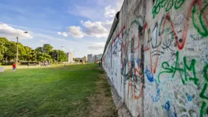 Die Berliner Mauer mit Graffiti trennt eine grüne Fläche von der Stadt.