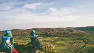 Zwei Personen sitzen bei einer Wanderung mit Blick auf die bayrische Berglandschaft.