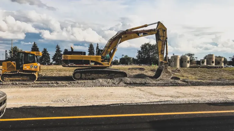 Gelber Bagger bei Bauarbeiten an einer Autobahnstrecke unter bewölktem Himmel.