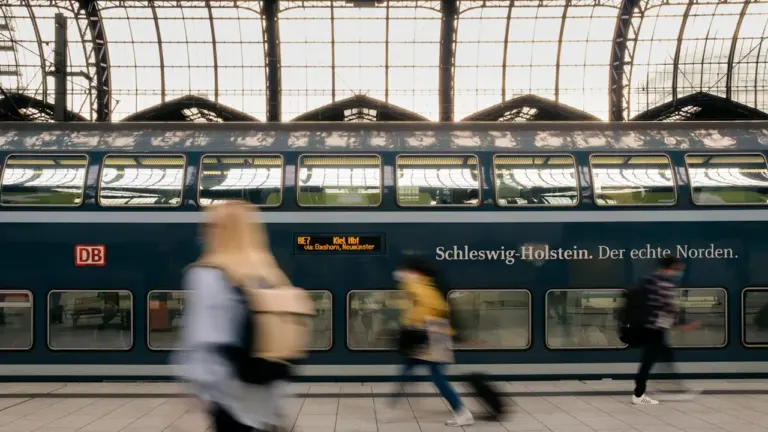 Ein roter Regionalzug der Deutschen Bahn fährt an einem grauen Tag in den Bahnhof.