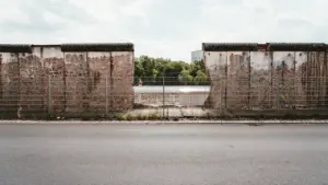 Ein grauer, roher Betonabschnitt der Berliner Mauer mit einem Durchlass vor Bäumen.