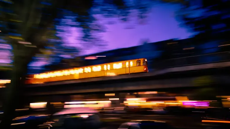 Gelbe Berliner U-Bahn fährt bei Dämmerung über eine erhöhte Strecke im Stadtzentrum.