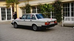 Ein klassischer weißer Oldtimer geschmückt mit rosa Bändern vor einem historischen Gebäude in Deutschland.