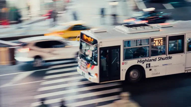 Ein weißer Bus fährt bei Bewegung durch einen belebten städtischen Zebrastreifen.