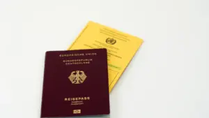 Ein deutscher Reisepass und ein gelber Impfpass liegen auf einem weißen Tisch.