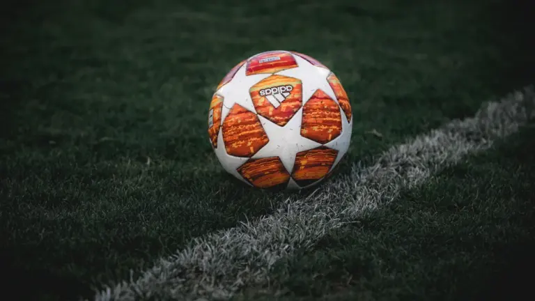 Ein Fußball liegt auf dem grünen Rasen an der weißen Seitenlinie des Spielfelds.