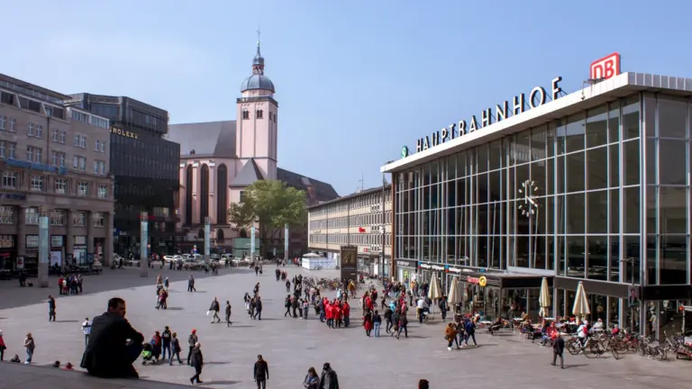 Blick auf den belebten Vorplatz des Kölner Hauptbahnhofs an einem sonnigen Tag.