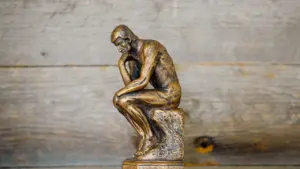 Eine bronzene Statue des Denkers vor einem rustikalen Hintergrund aus Holz.