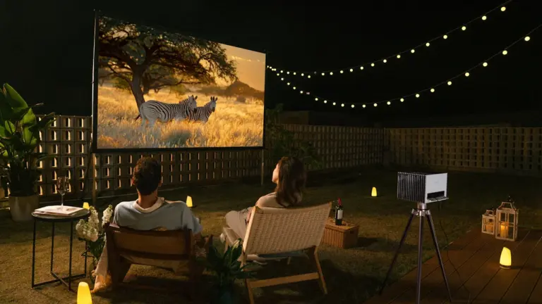 Paar genießt abends einen Film bei einem privaten Open-Air-Kino im Garten mit Lichterkette.