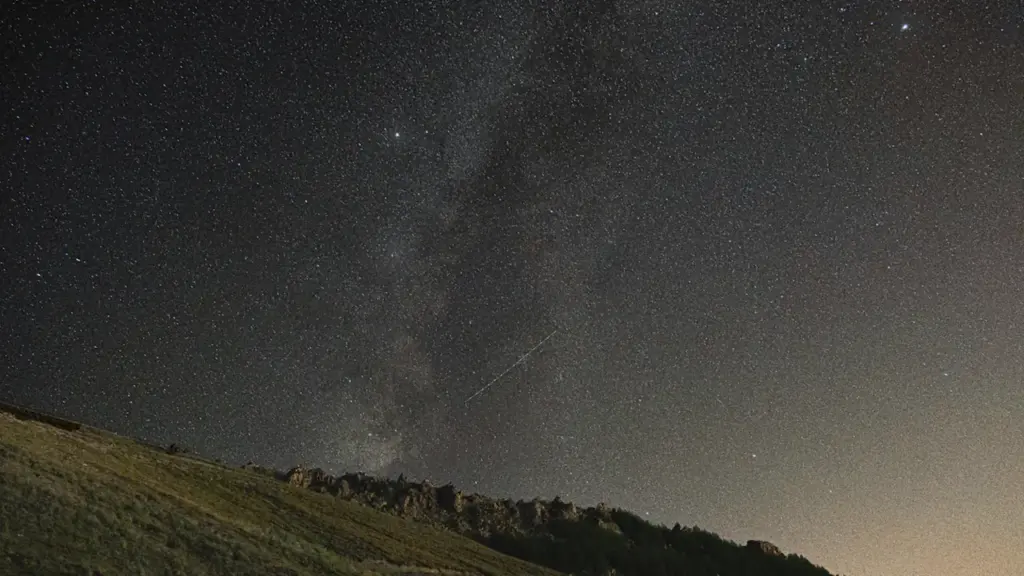 Sternenhimmel über einem grasbewachsenen Hügel in einer klaren, dunklen Nacht.