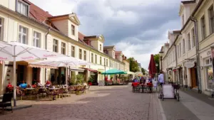 Historische Häuserzeile mit Straßencafés in der Innenstadt von Potsdam bei bewölktem Himmel.