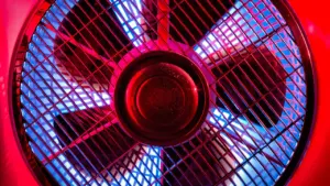 Ein Ventilator steht auf einem Holztisch bei stimmungsvoller Beleuchtung in einem Innenraum.