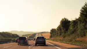 Autoverkehr auf einer deutschen Autobahn bei sonnigem Wetter und sanften Hügeln im Hintergrund.