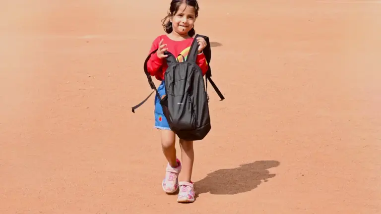 Ein junges Mädchen mit Schulrucksack läuft über einen hellen, sandigen Untergrund im Freien.