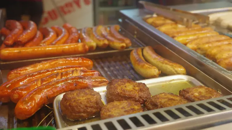 Verschiedene Bratwürste und Fleischfrikadellen in einer Auslage auf einem Markt in Deutschland.