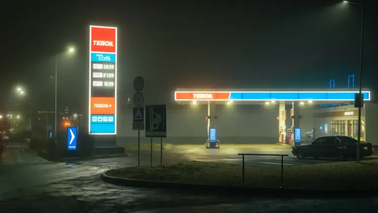 Eine beleuchtete Tankstelle in nebliger Nachtatmosphäre mit deutlich sichtbaren Preistafeln an der Straße.