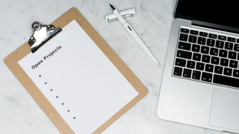 Ein Klemmbrett mit der Aufschrift Open Projects neben einem silbernen Laptop auf Marmor.