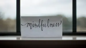 Ein Blatt mit der Aufschrift Mindfulness liegt nachdenklich vor einem großen Fenster.