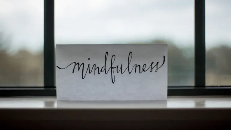 Ein Blatt mit der Aufschrift Mindfulness liegt nachdenklich vor einem großen Fenster.