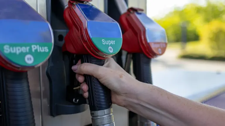 Nahaufnahme einer Hand beim Halten einer Zapfpistole an einer Tankstelle.
