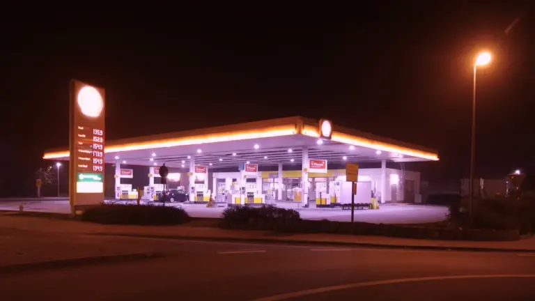 Eine nächtlich beleuchtete Tankstelle mit Preisanzeige und wartenden Autos an der Zapfsäule.