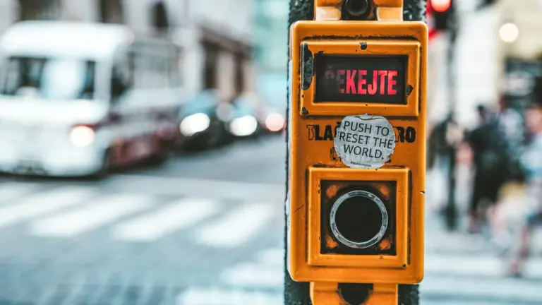 Gelber Fußgänger-Ampelschalter an einer vielbefahrenen Straße mit einem Aufkleber.
