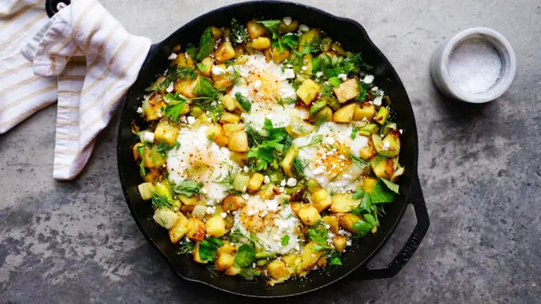Eine gusseiserne Pfanne mit gebratenem Gemüse, frischen Kräutern und zerbröckeltem Feta-Käse.