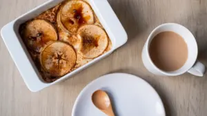 Ein Apfel-Hafer-Auflauf in einer Auflaufform neben einer Tasse Kaffee auf einem Holztisch.