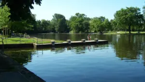 Ein langer Betonsteg ragt in einen ruhigen See, umgeben von grünen Bäumen an einem Sommertag.