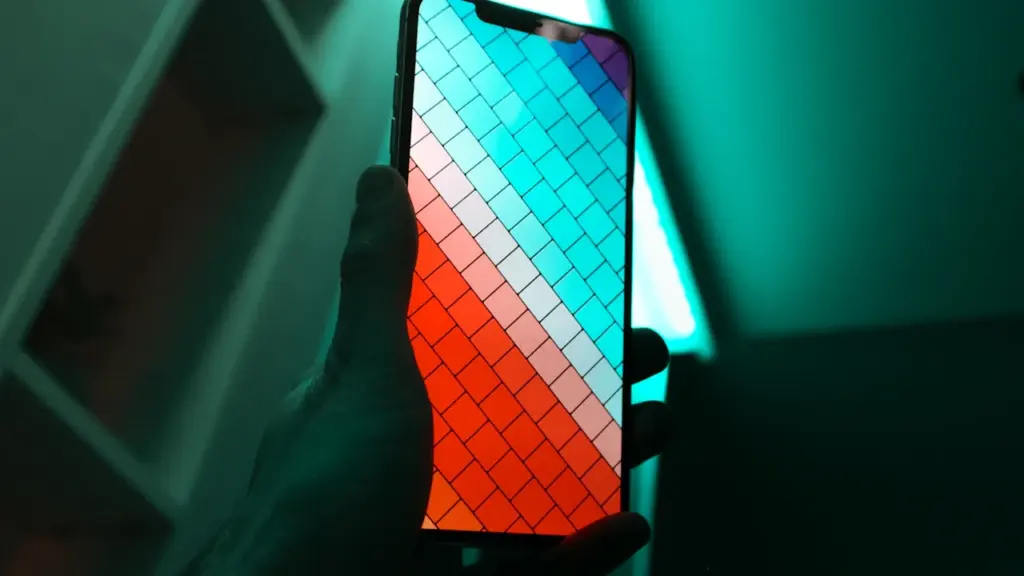 Eine Hand hält ein Smartphone mit leuchtendem Bildschirm in dunkler Umgebung.