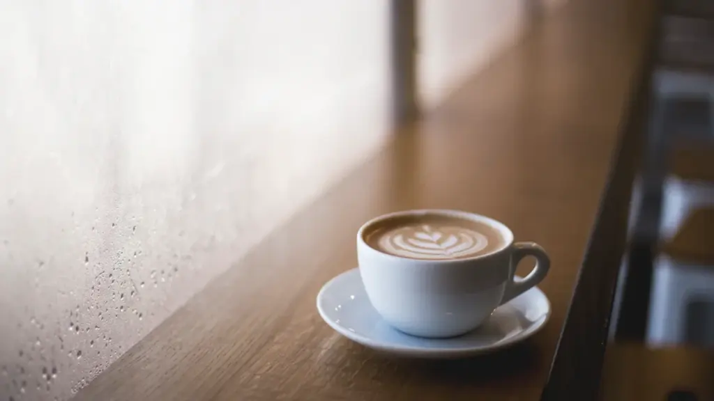 Eine Tasse frisch gebrühter Kaffee auf einem Holztisch neben einem Fenster bei Tageslicht.