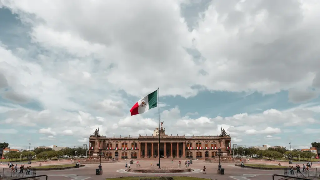 Die mexikanische Flagge weht stolz vor einem historischen Gebäude unter bewölktem Himmel.