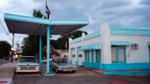 Historische Tankstelle mit Zapfsäulen und klassischen Autos unter einem blauen Vordach