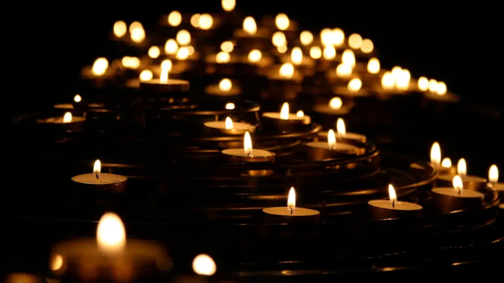 Viele brennende Kerzen in einer dunklen Kirche, symbolisch für Trauer und Gedenken.