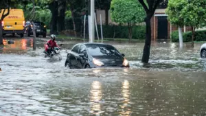 Ein schwarzes Auto fährt durch eine überschwemmte Straße bei starkem Regen in einer Stadt.