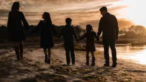 Eine Familie spaziert bei stimmungsvollem Sonnenuntergang gemeinsam am Strand entlang.