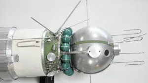 Ein historisches Modell des sowjetischen Sputnik-Satelliten mit runder Metallkapsel und hervorstehenden Antennen vor weißem Hintergrund.