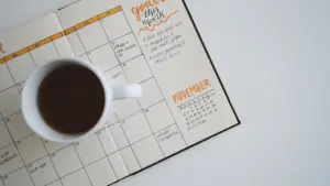 Eine weiße Kaffeetasse steht auf einem Kalender für die tägliche Planung bereit.